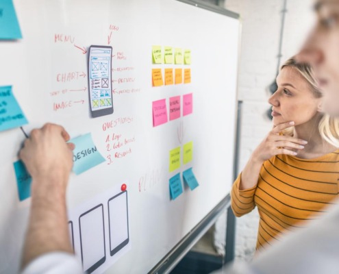 A female designer is looking at the whiteboard. There are prototype designs and sticky notes on the board.